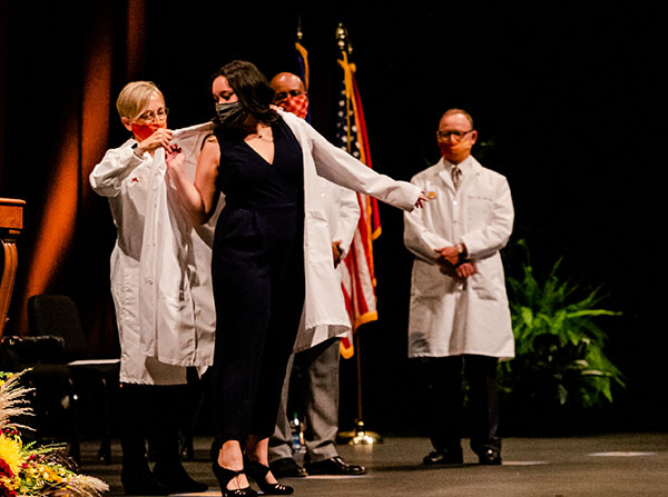 Second year student receives her White Coat from Dr. Cyndee Stull as Dean Keith Mays looks on.