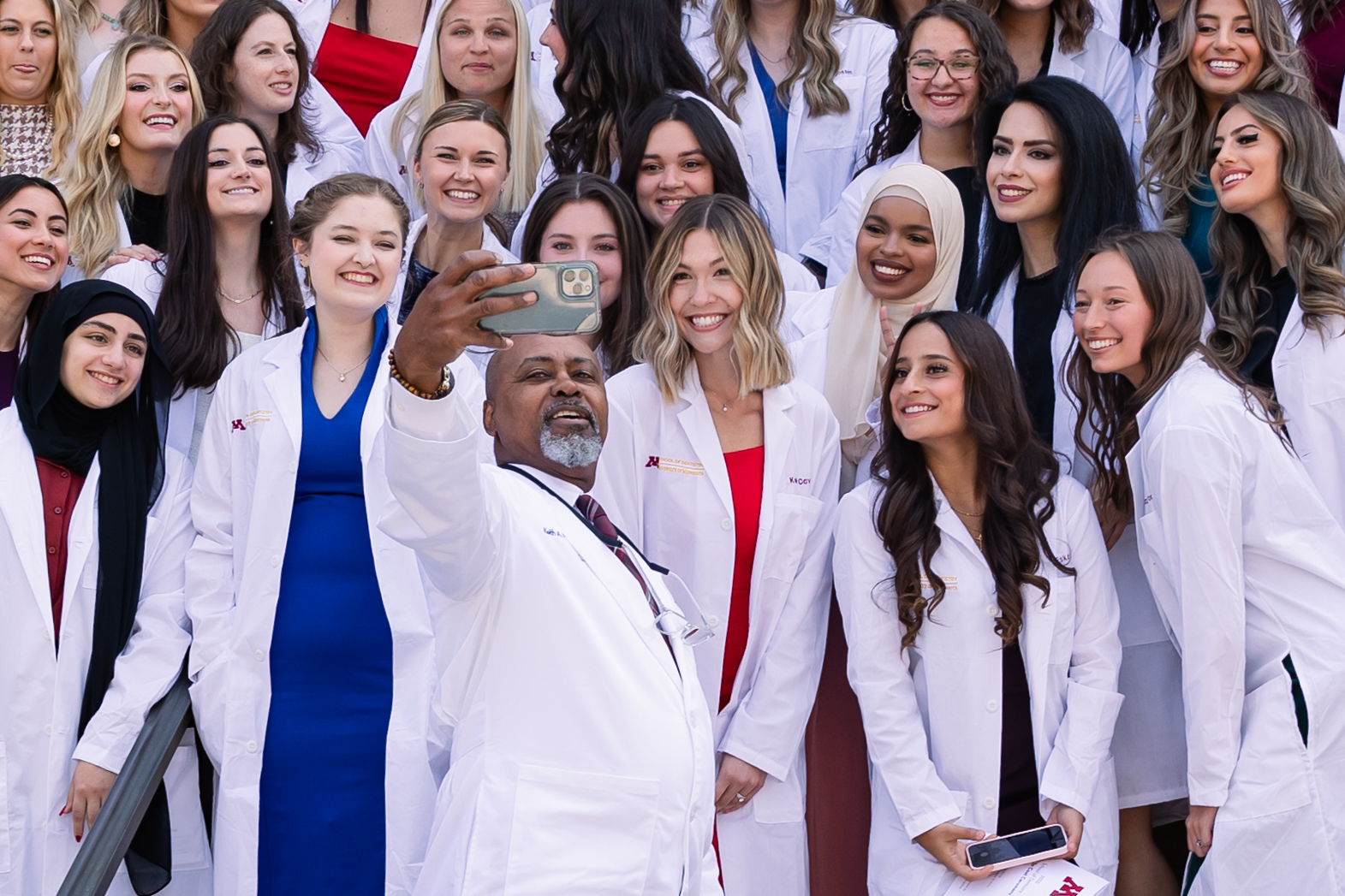 Dean Mays takes a selfie with a group of DDS students in white coats