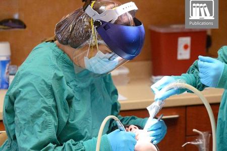 Dentist in scrubs and PPE working on patient