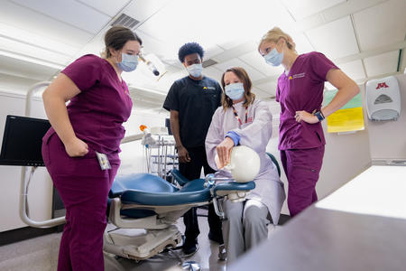Dental hygiene and therapy learners watch a faculty member demonstrate technique on a typodont