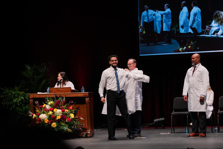 A student smiles as he receives his white coat on stage