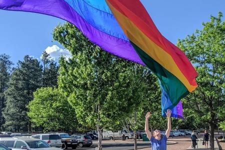Robert Springer raises his hands toward a Pride flag