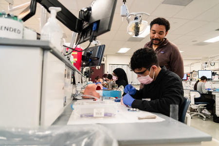 Isaac Tade oversees a Discover Dental School student working in the preclinic