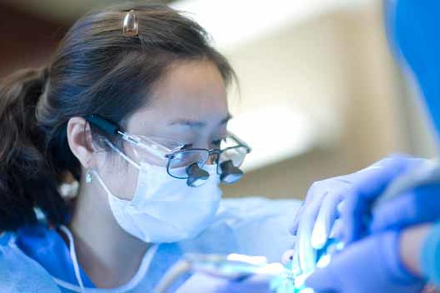 female dentists with eyeglasses and magnifiers works on patient