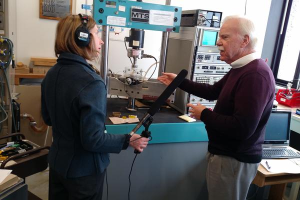 researcher being interviewed in lab by woman wearing headphones and holding large microphone