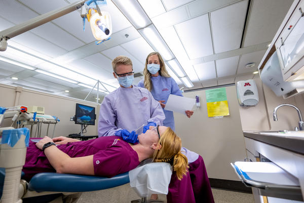dental hygiene student inspects the mouth of a fellow student in a clinic demonstration