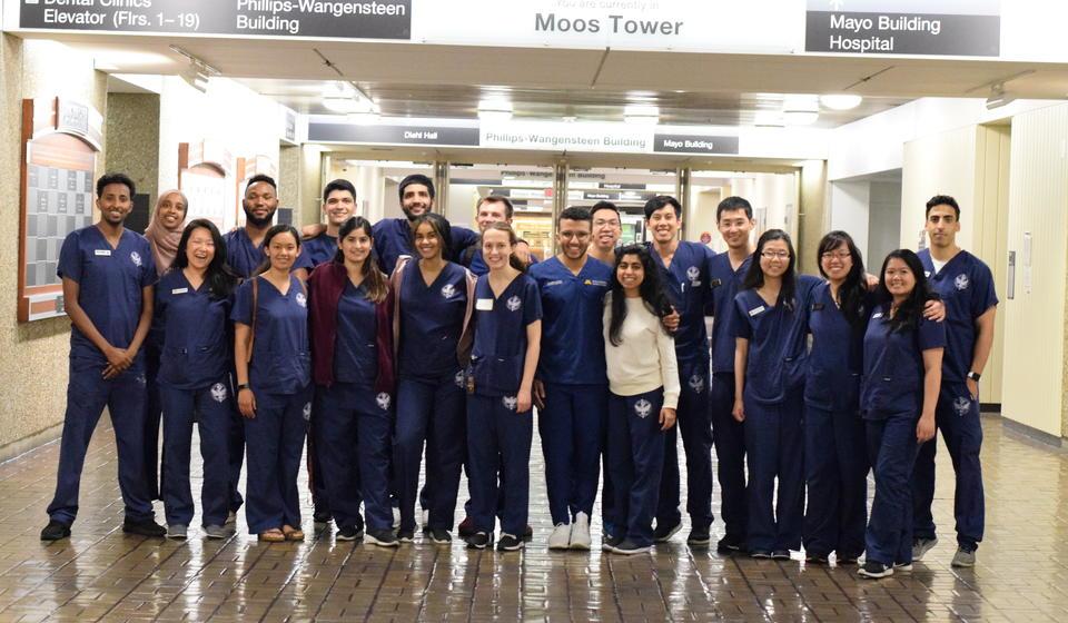 approx. 30 dental school students posed in hall wearing dark blue scrubs
