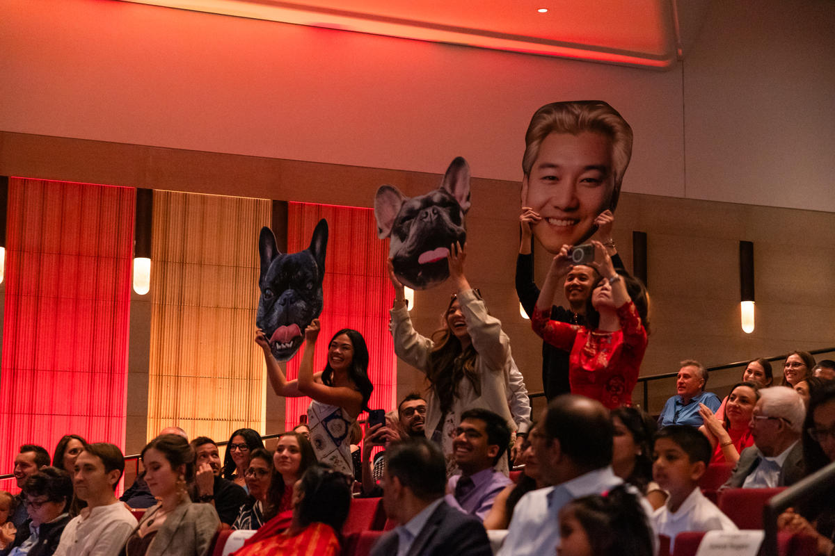 Guests hold up cutouts of a graduate and his dogs from the audience