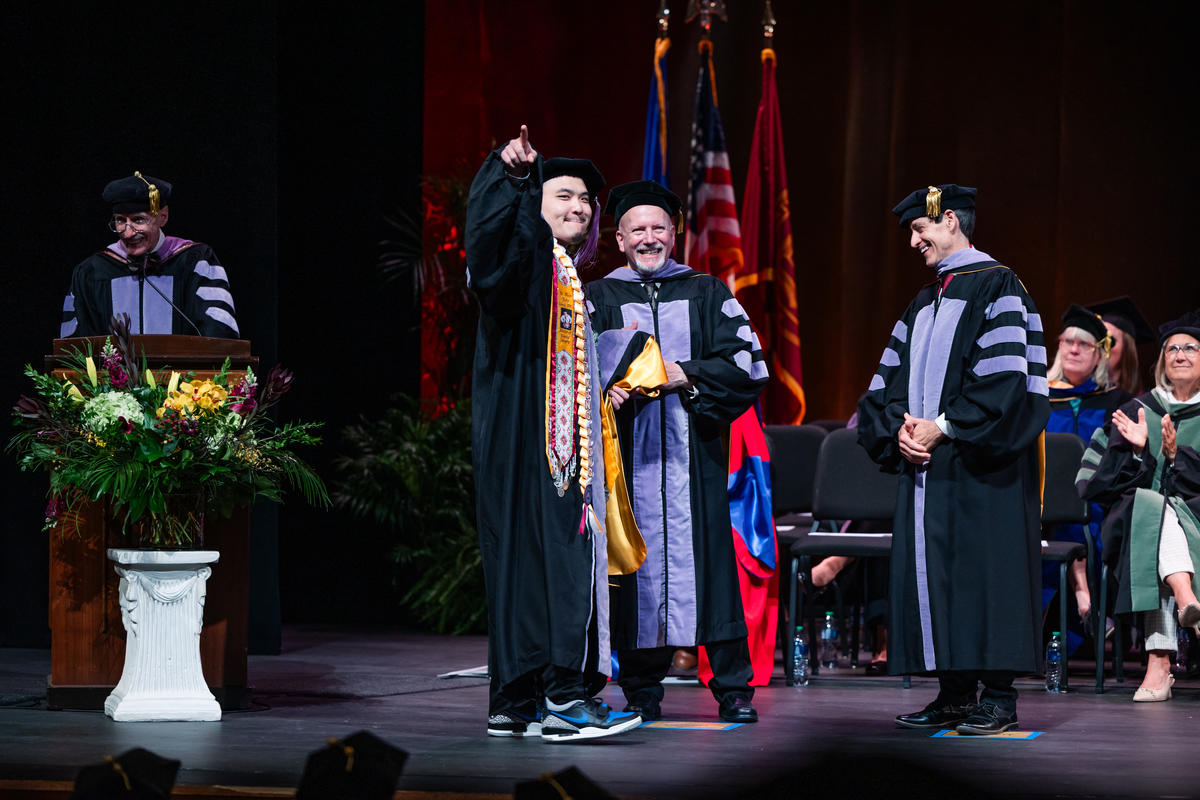A graduate is hooded onstage and points to an audience member