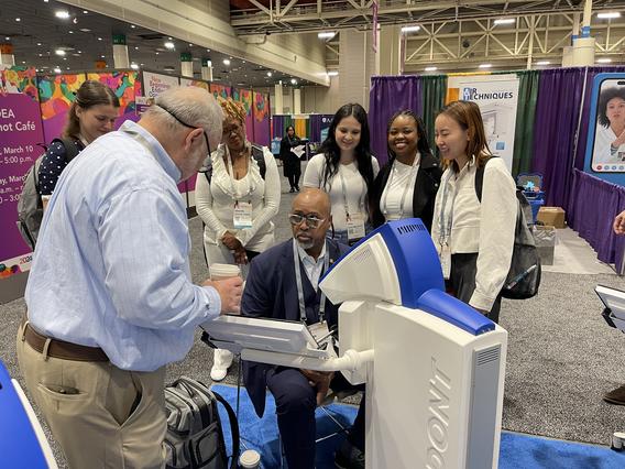 Dean Keith Mays partakes in an exhibition at a booth at the ADEA Annual Session while students observe