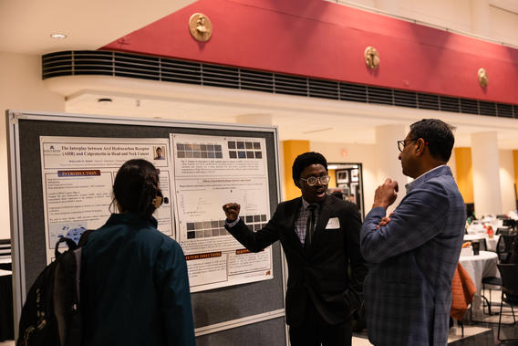 A student shows his research poster to faculty and attendees at Research Day 2024