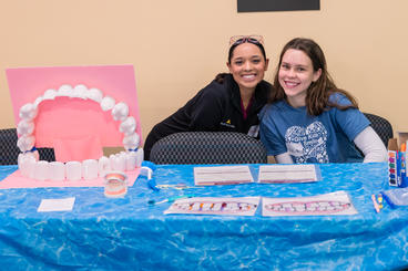Dental hygiene students sit at a table with teeth cleaning information