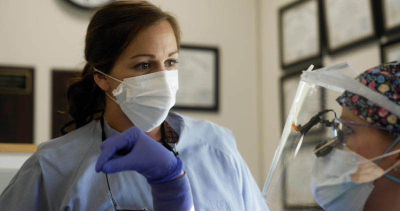 A dentist listens to a dental student in clinic
