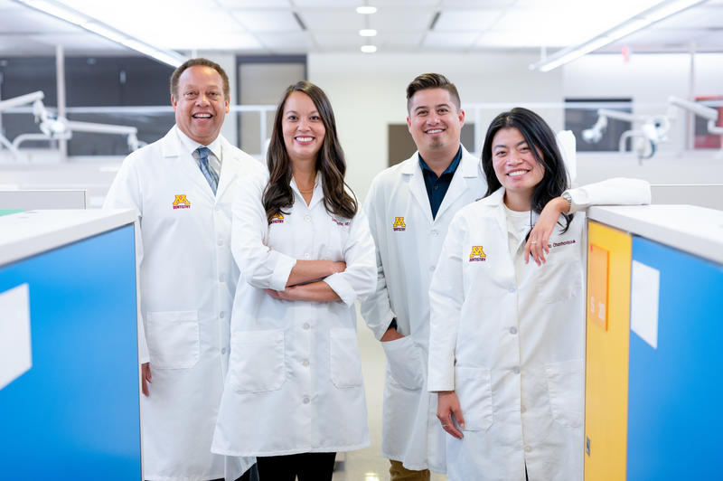 Karl Self, Danae Seyffer, Drew Christianson, and Phonsuda Chanthavisouk smile and pose in a pre-clinical area with lab coats on.