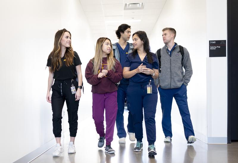 group of five dental students in scrubs and sweaters walking down a hallway talking