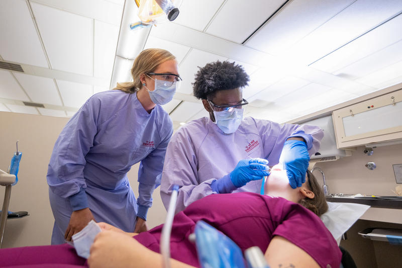 Two dental hygiene students work on another student as a patient