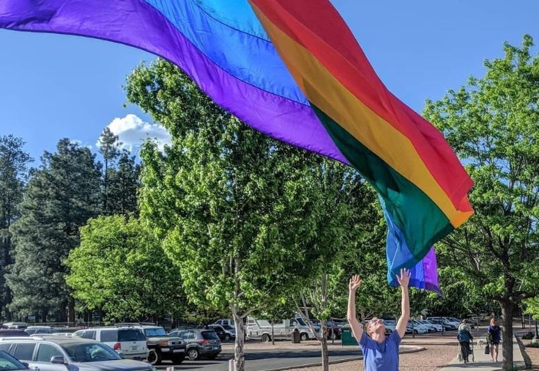 Robert Springer raises his hands toward a Pride flag