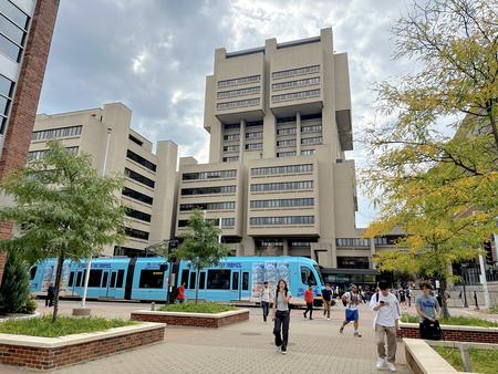 Malcom Moos Health Sciences Tower with light rail train and students 2023